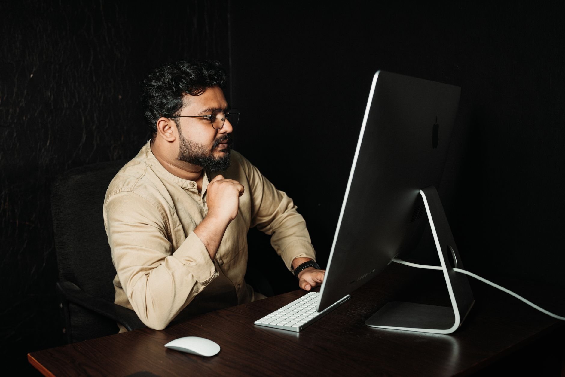 A man is focused on his work at a desk in an office setting, using a modern computer.